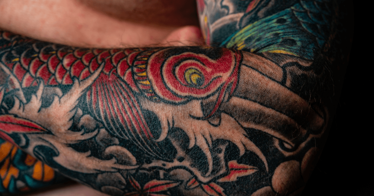 A man showcasing his tattooed arm, displaying intricate designs and vibrant colors.